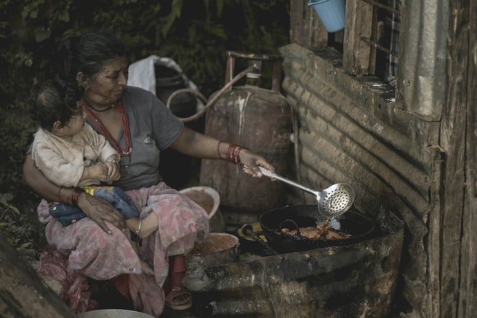 Photo of a woman cuddling her child while cooking on a pressurised kerosene stove in Nepal